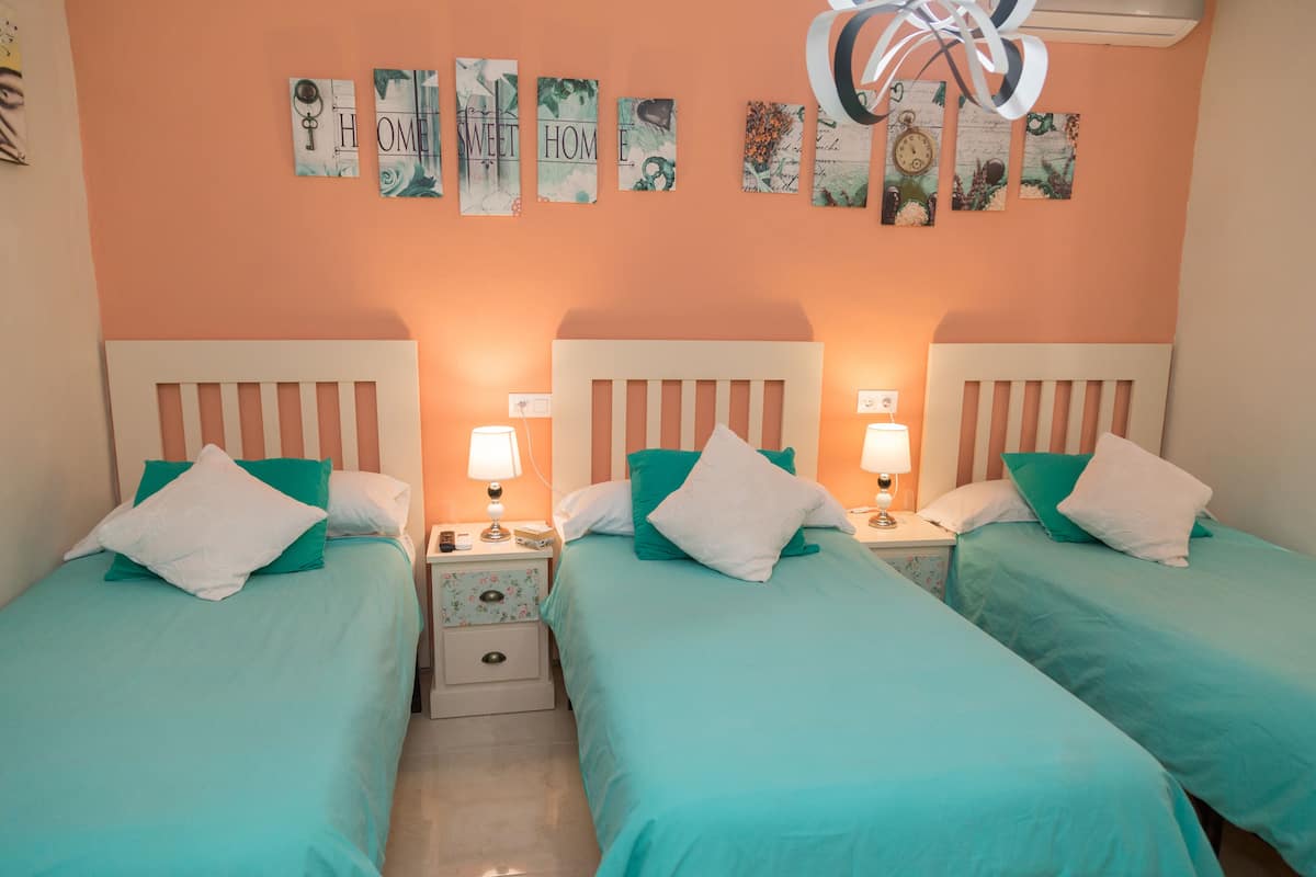 A room with two beds, each with a white headboard and teal bedding. There are two bedside tables with lamps, and a wall decorated with framed pictures.