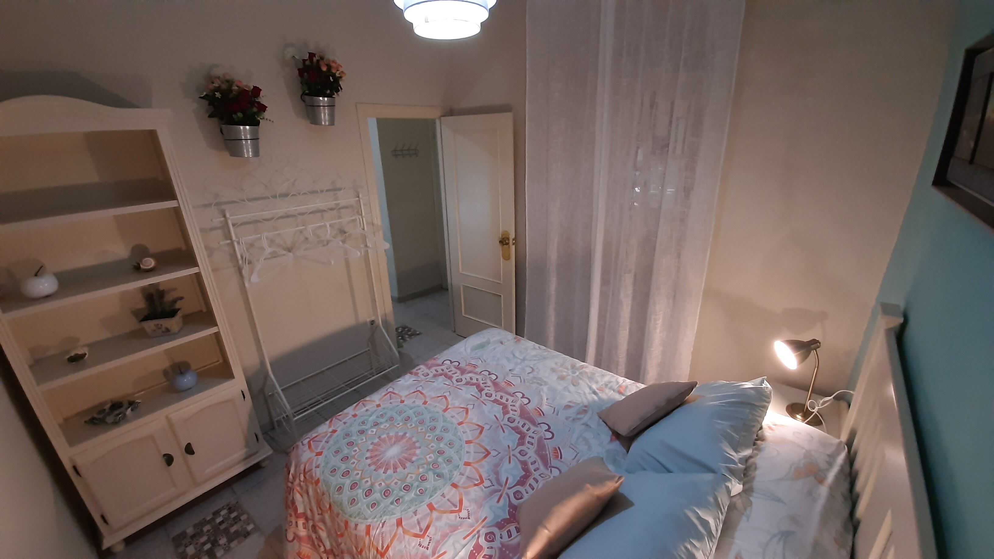 Une chambre à coucher avec un lit, une armoire, un miroir et une plante suspendue.