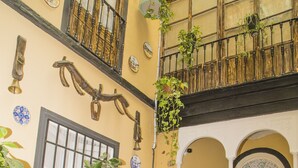 A courtyard with a fountain, wicker chairs, a table with a plant, and a balcony with plants. - Pension Internacional (Córdoba)