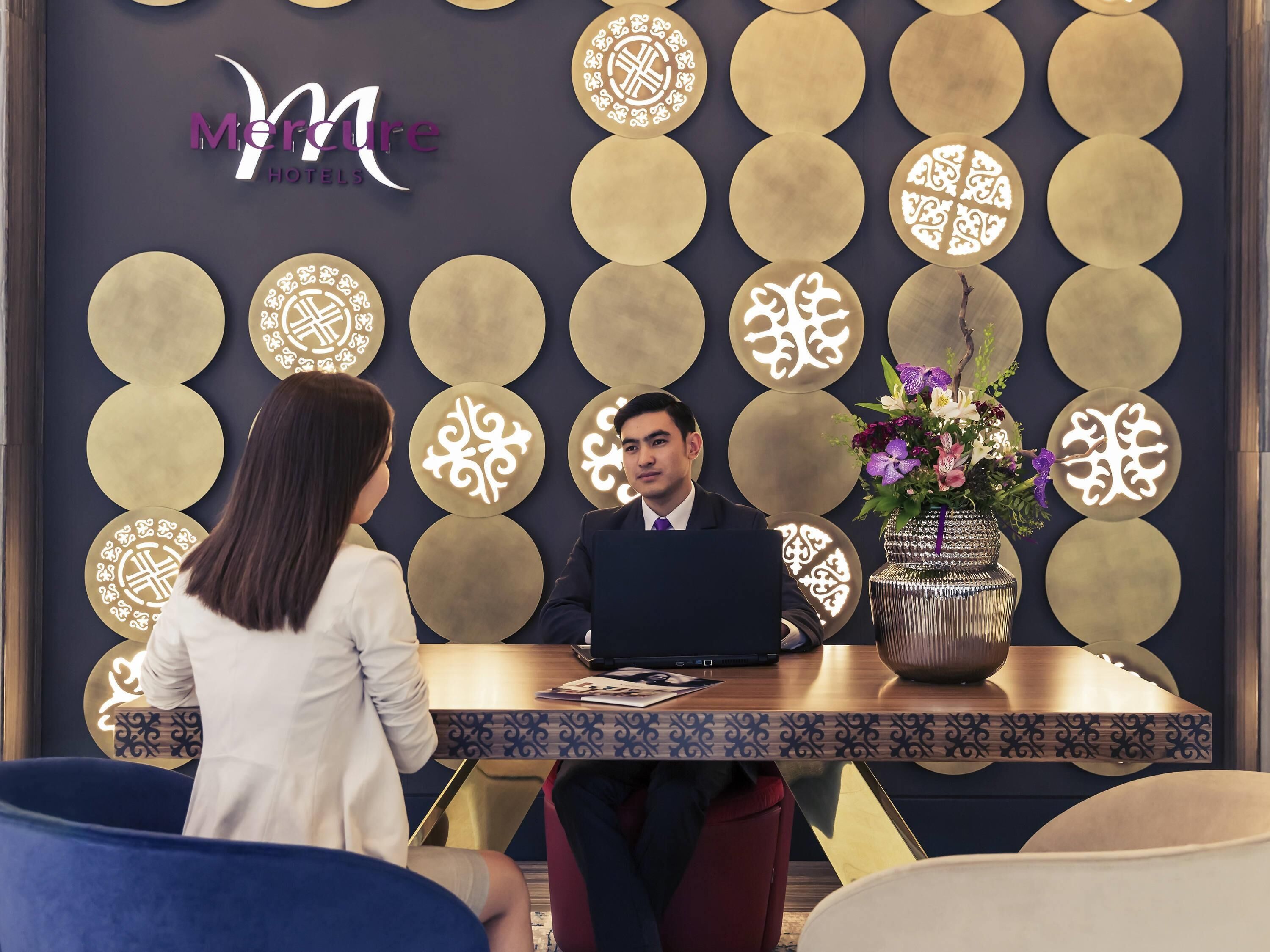 A reception desk with a logo, a patterned wall, and a vase with flowers.