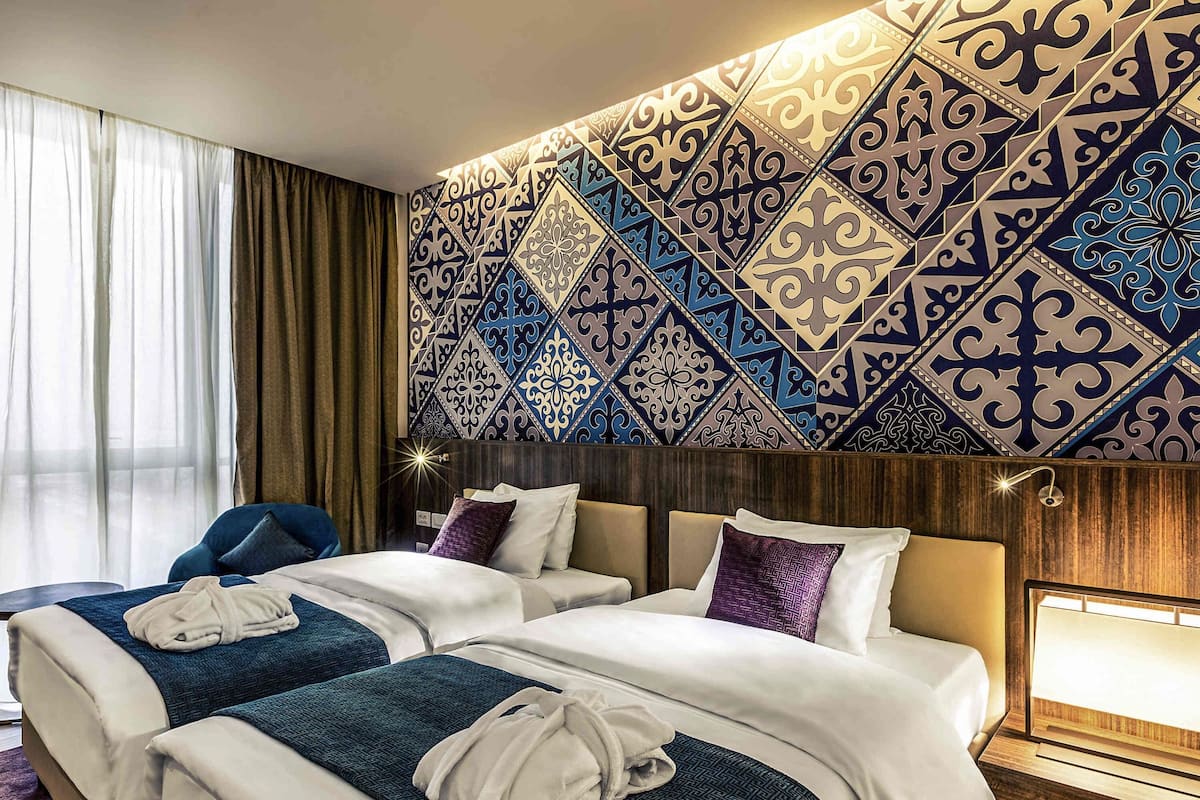 Una habitación de hotel con dos camas, un ventanal con cortinas y un papel tapiz estampado.