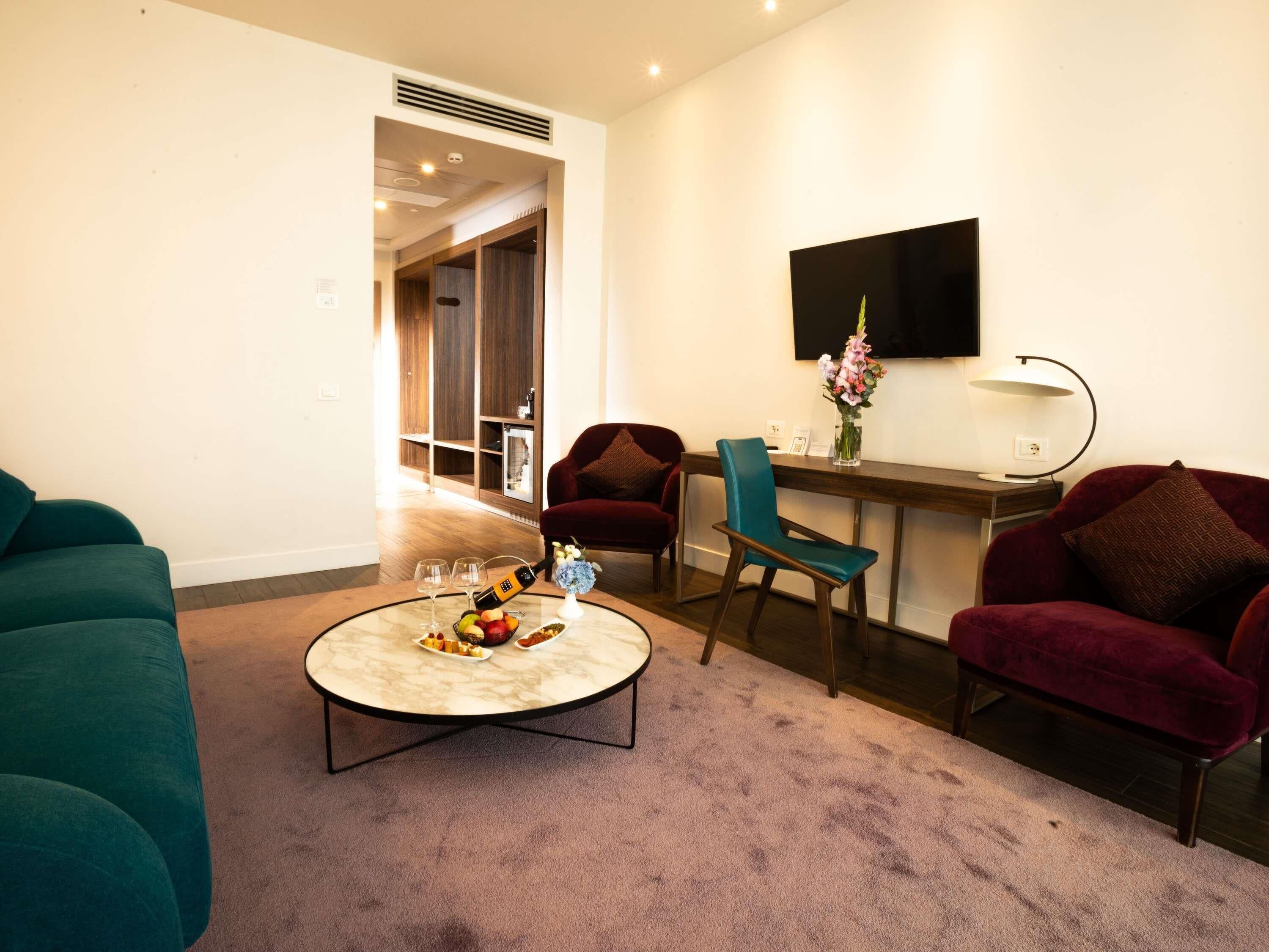 Una sala de estar moderna con una mesa redonda, dos sillones, un televisor montado en la pared y un mueble de madera.