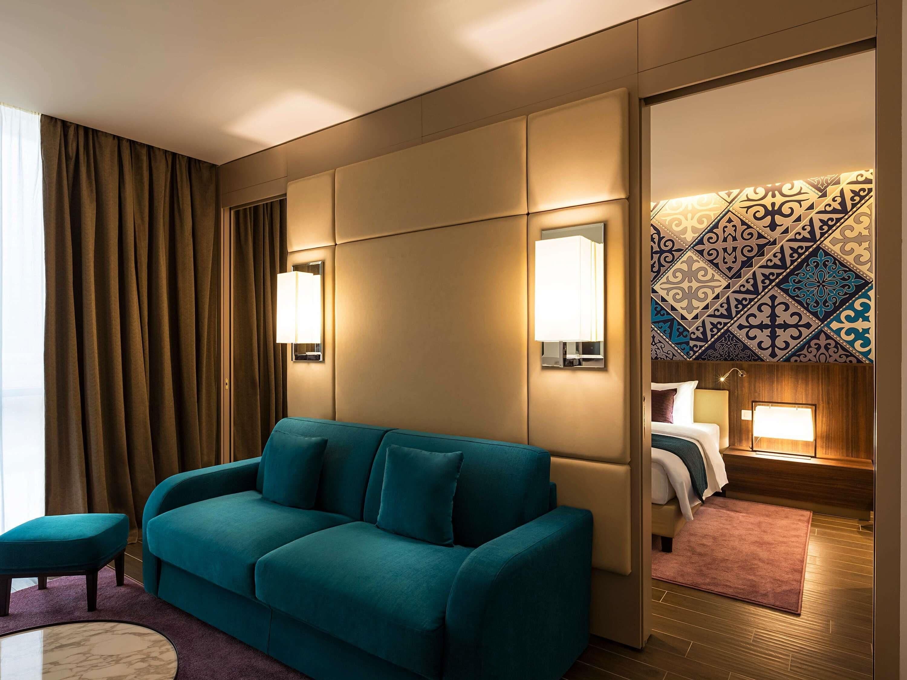 A hotel room with a teal sofa, a small round table, a mirror, and a patterned wall.
