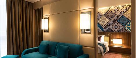 A hotel room with a teal sofa, a small round table, a mirror, and a patterned wall.