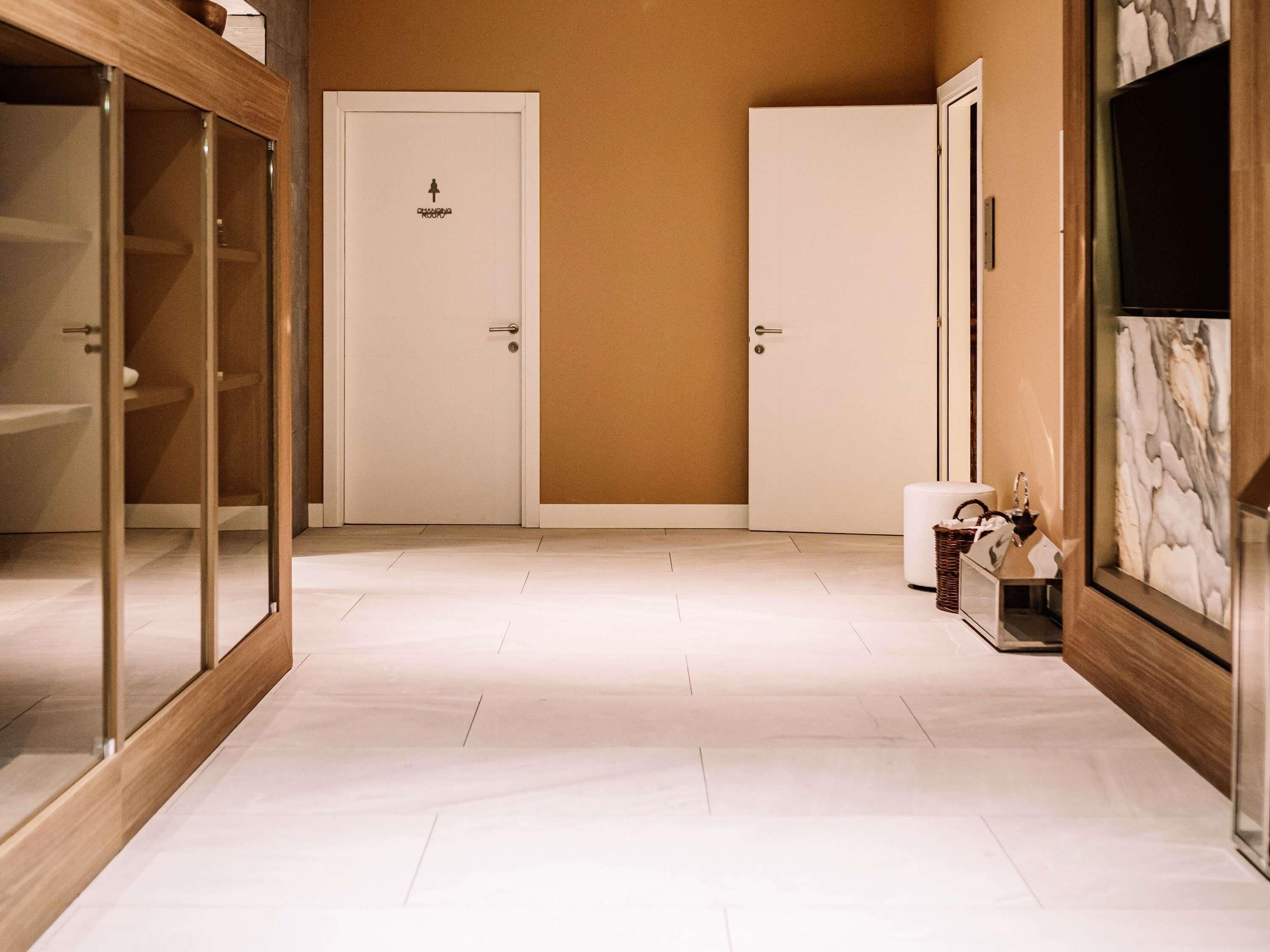 Un pasillo con dos puertas blancas, un aparador de vidrio con marco de madera y una pared con diseño de mármol.