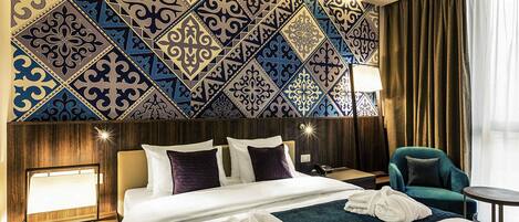 Una habitación de hotel con una cama grande, una mesita de noche, una lámpara, una silla y una pared con diseño.