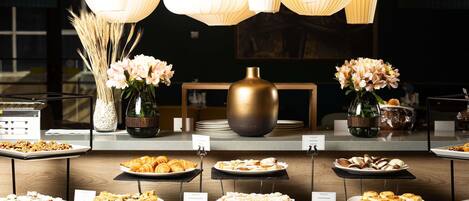 A buffet setup with various food items, a vase with flowers, and hanging light fixtures.
