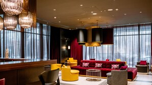 A modern hotel lobby with a red sofa, yellow chairs, and a bar area. - Mercure Almaty City Center (Almaty)