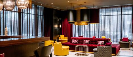 A modern hotel lobby with a red sofa, yellow chairs, and a bar area.