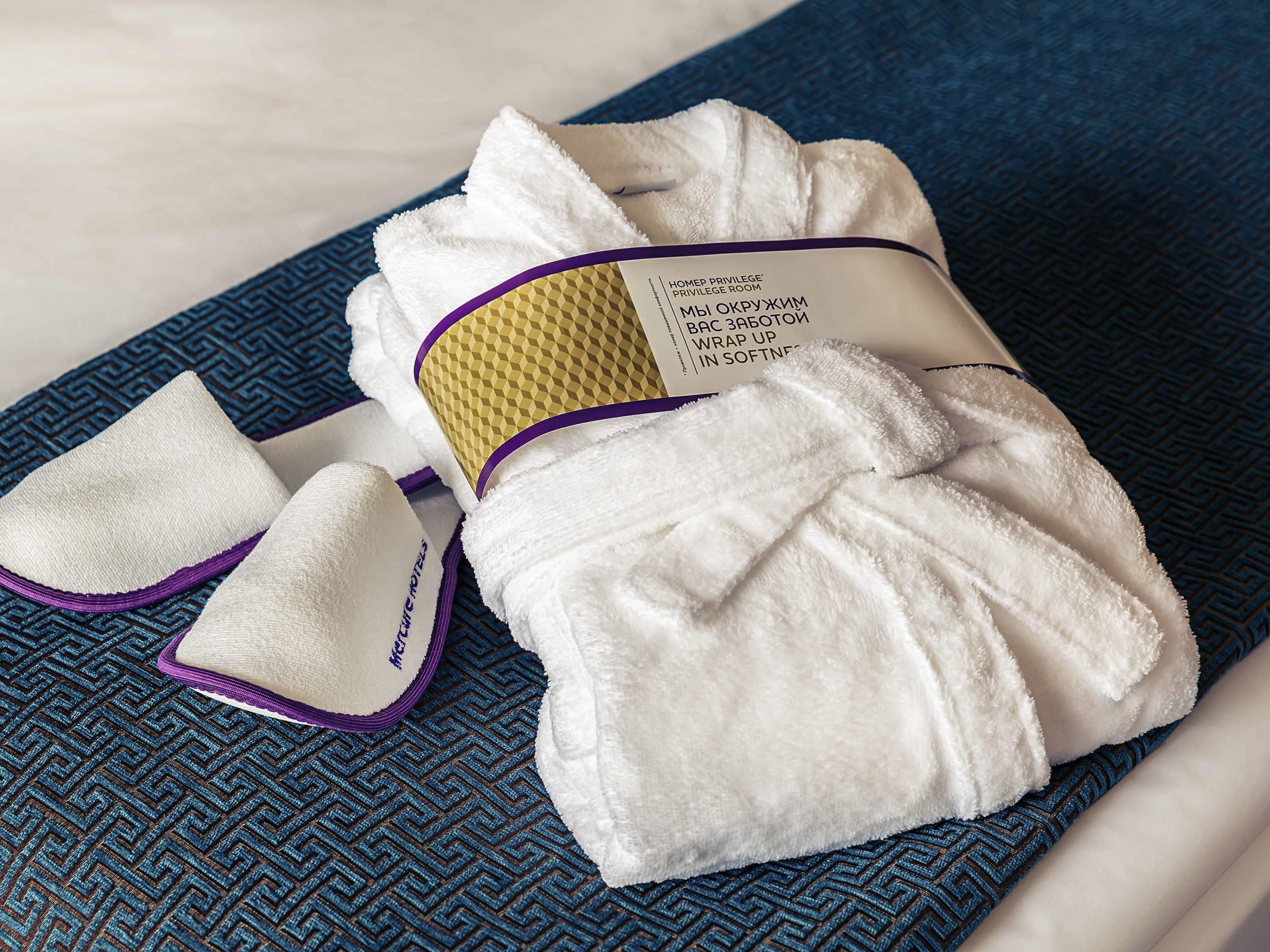 A neatly folded white towel and two white footmasks with purple trim, placed on a blue patterned bedspread.