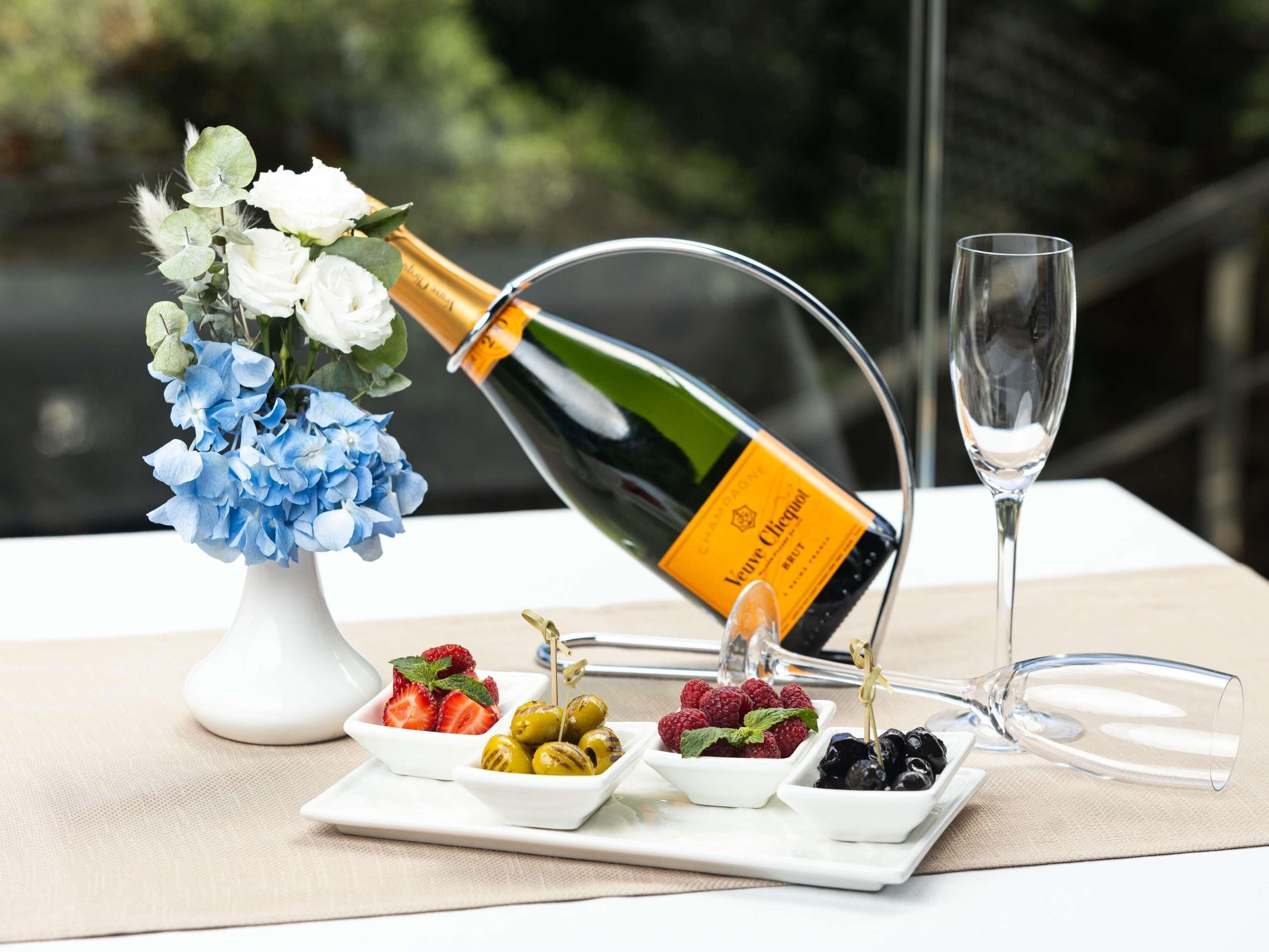 Una botella de champán, una copa, una mesa con fruta y flores.
