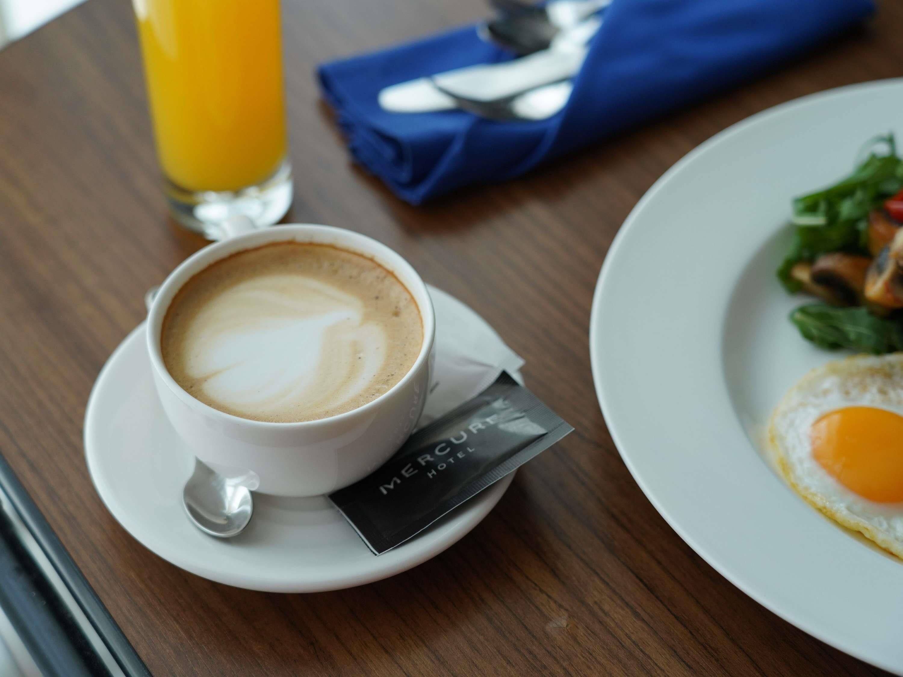 A table with a cup of coffee, a glass of orange juice, a plate with a fried egg, and a napkin.