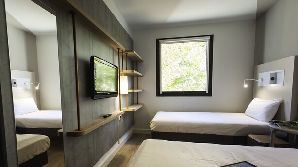 Une chambre d’hôtel moderne avec deux lits, une télévision, une fenêtre donnant sur un beau paysage et une table de chevet avec une lampe.