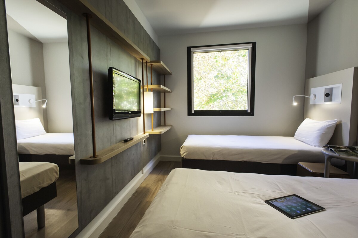 Une chambre d’hôtel moderne avec deux lits, une télévision, une fenêtre donnant sur un beau paysage et une table de chevet avec une lampe.