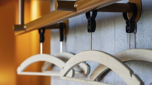 Un gros plan d’un porte-vêtements en bois muni de plusieurs cintres, fixé à une tige métallique, le tout adossé à un mur texturé.