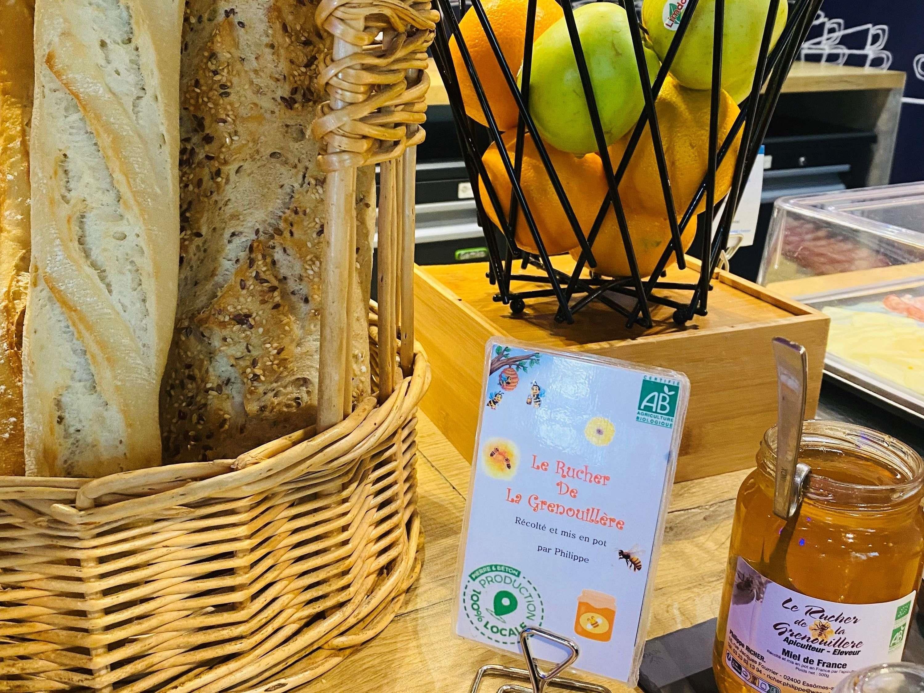 A wicker basket with baguettes, a basket of apples, and a jar of honey.