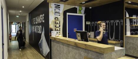 A reception desk with a wooden counter and a computer monitor. There is a blue door behind the desk, and a wall with a large poster.