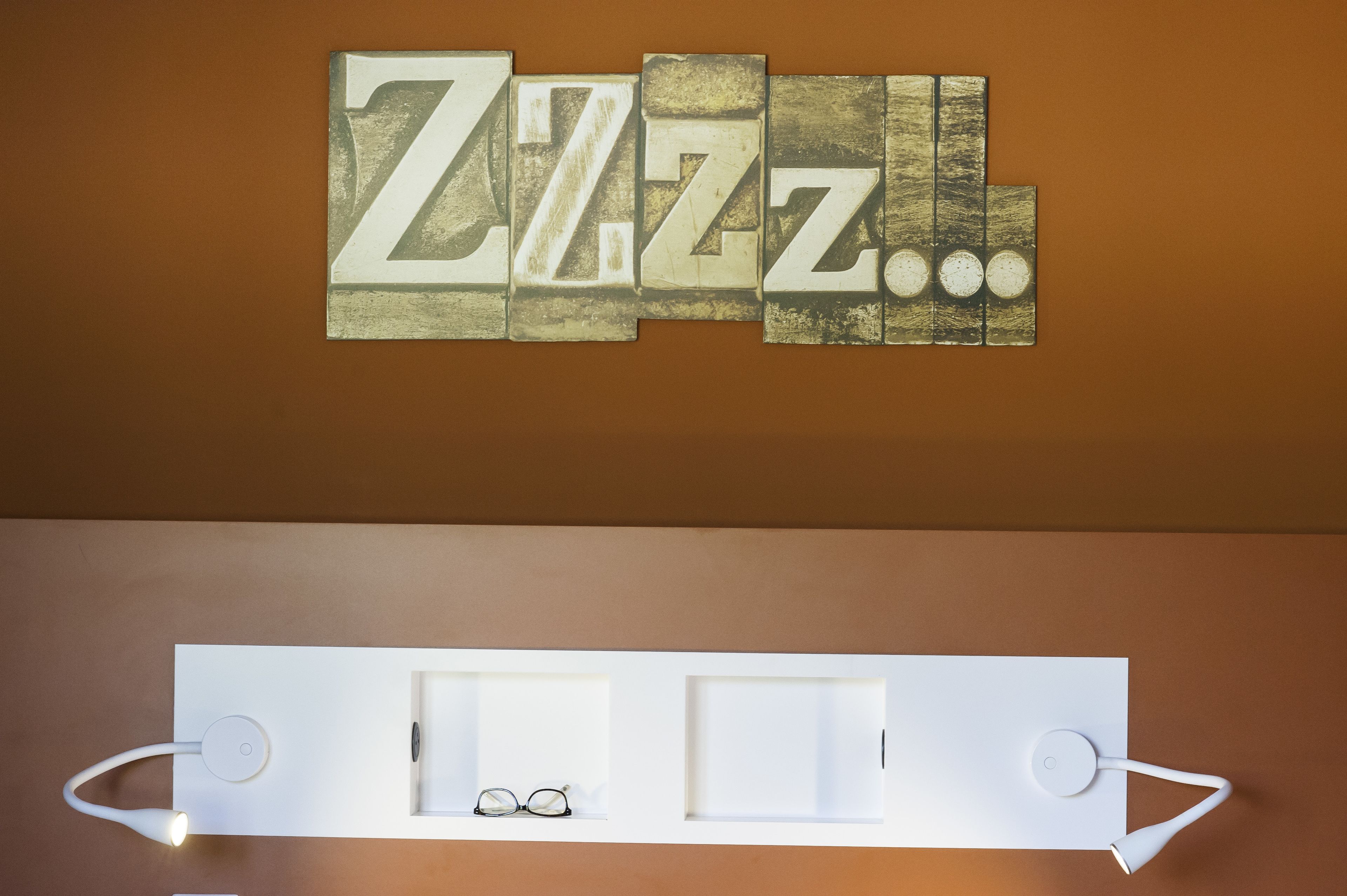 A wall with the word "ZIZZ" in large letters and a white shelf below with glasses and a small item.