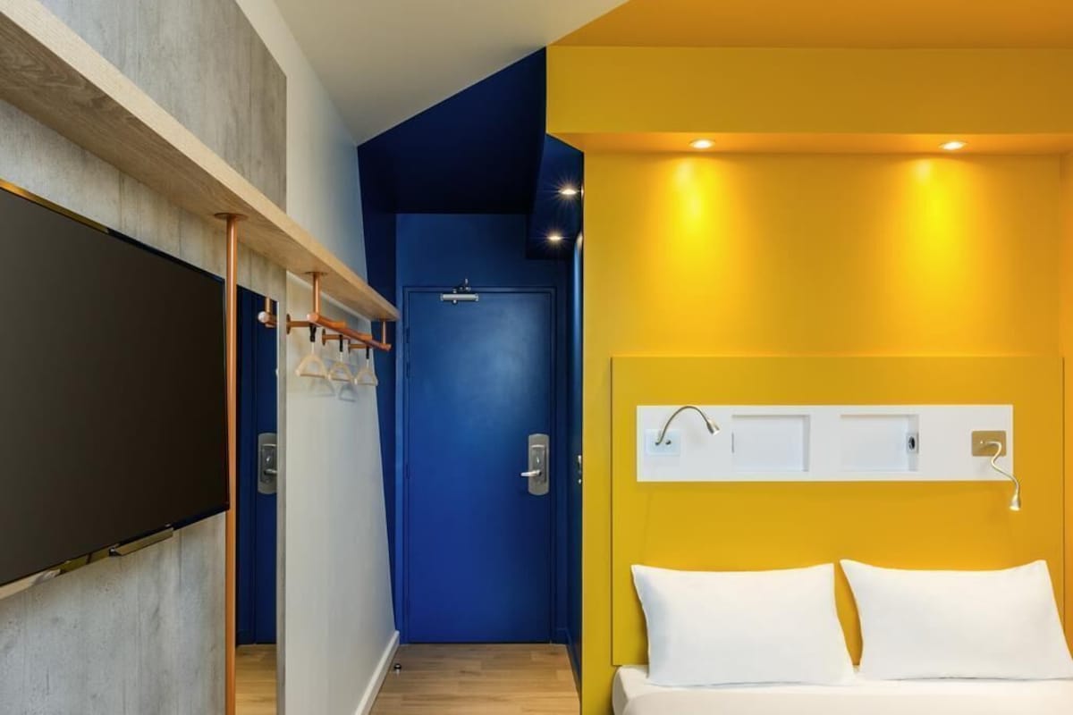 Une chambre d’hôtel avec un lit, une porte et un téléviseur fixé au mur.