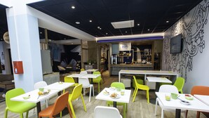Een modern restaurant met witte tafels en stoelen, een toonbank met een menu en een muur met abstracte ontwerpen.