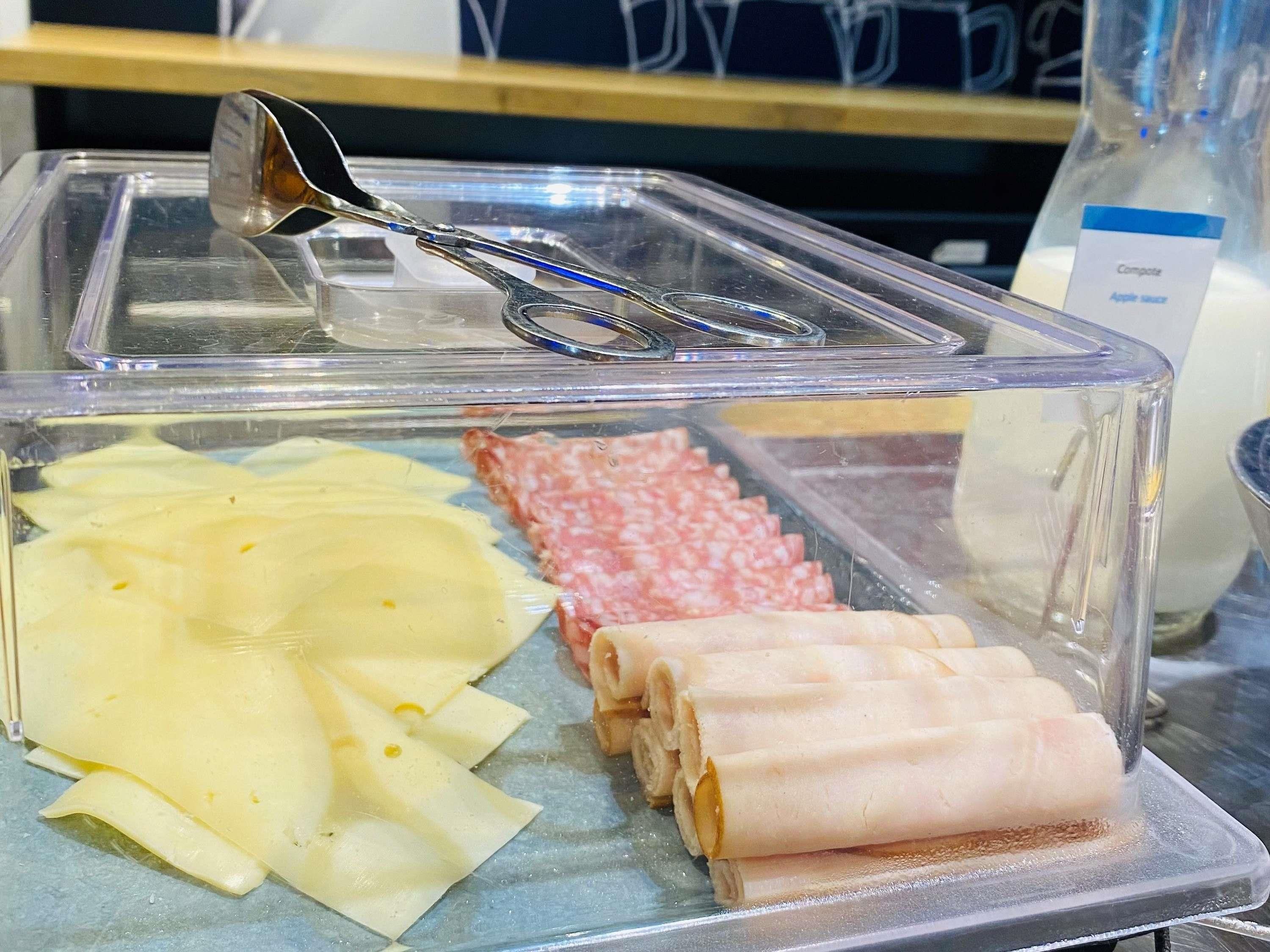 Exhibición de alimentos con queso en rodajas, embutidos y una botella de jugo de manzana.