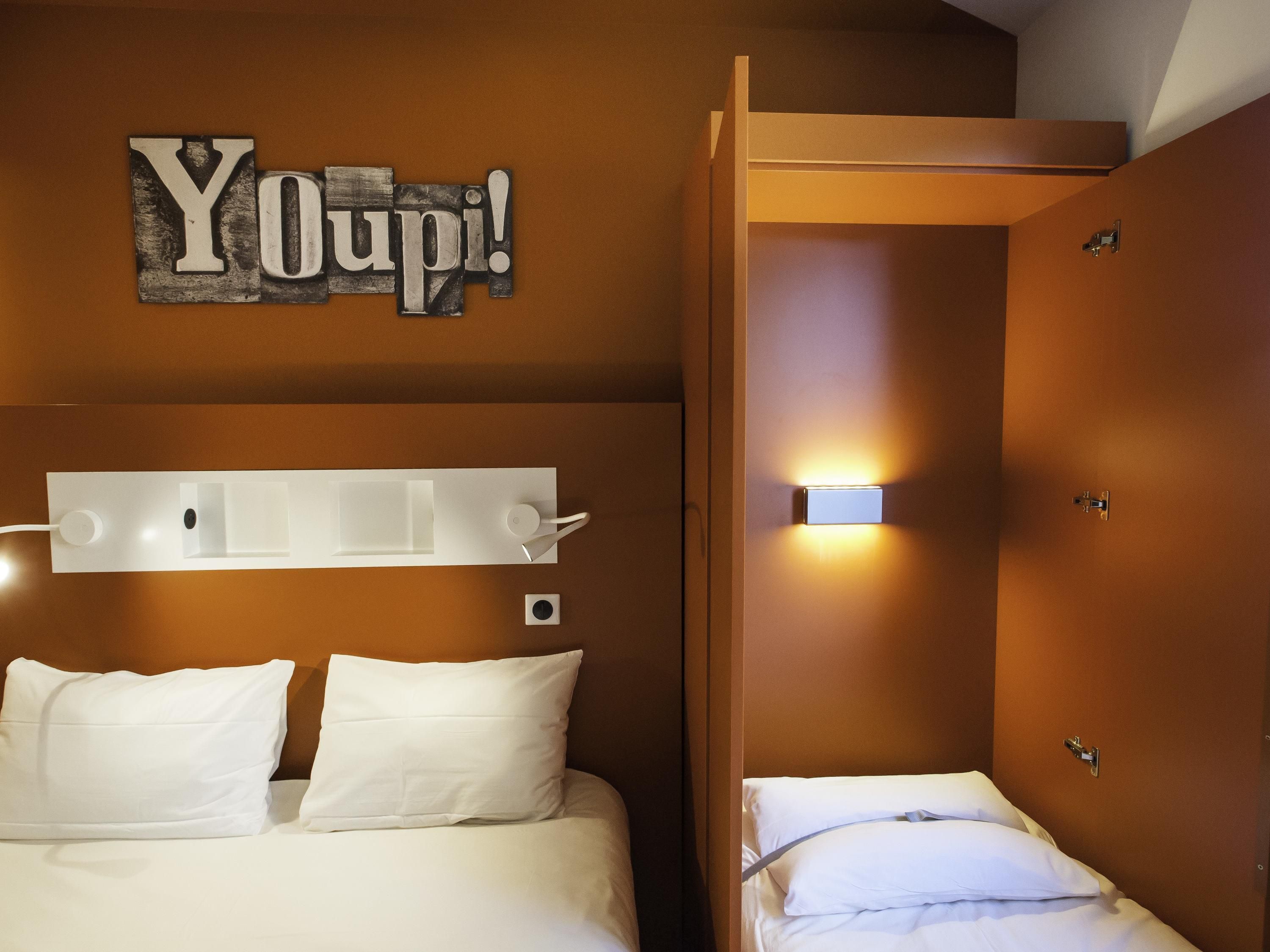 Ett hotellrum med en säng, ett sängbord, en väggmonterad lampa och en dörr.