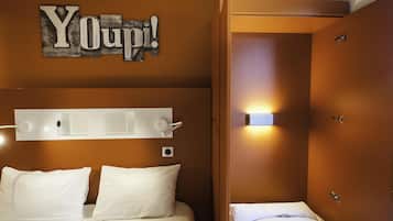 A hotel room with a bed, a bedside table, a wall-mounted light, and a door.