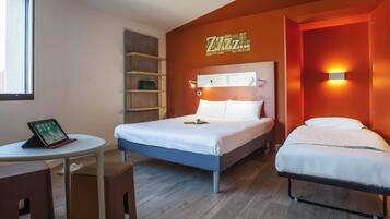 A hotel room with a bed, bedside tables, a desk with a tablet, and a wall-mounted shelf.