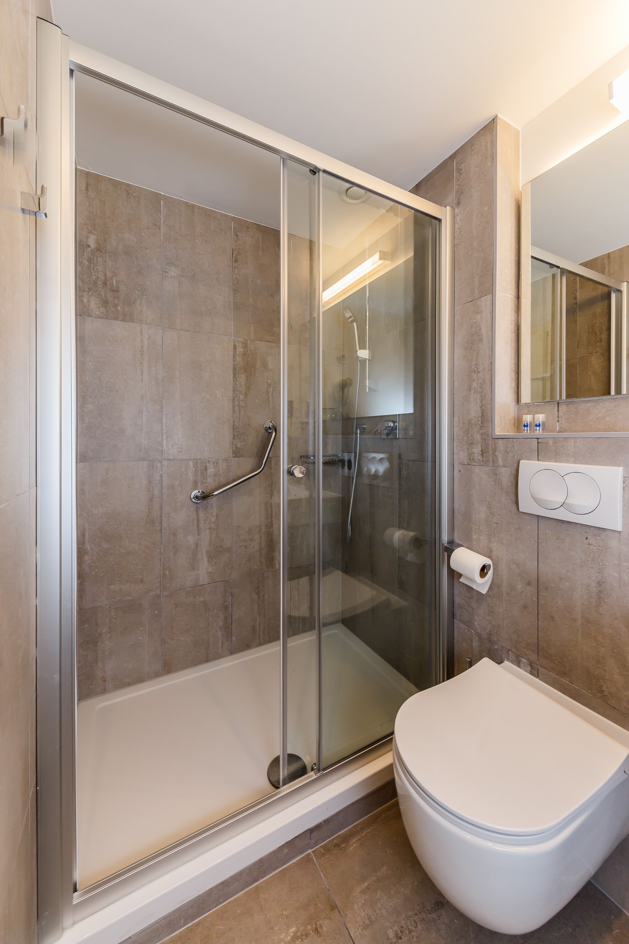 Een moderne badkamer met een douche in een glazen cabine, een wit toilet en een wandcloset.