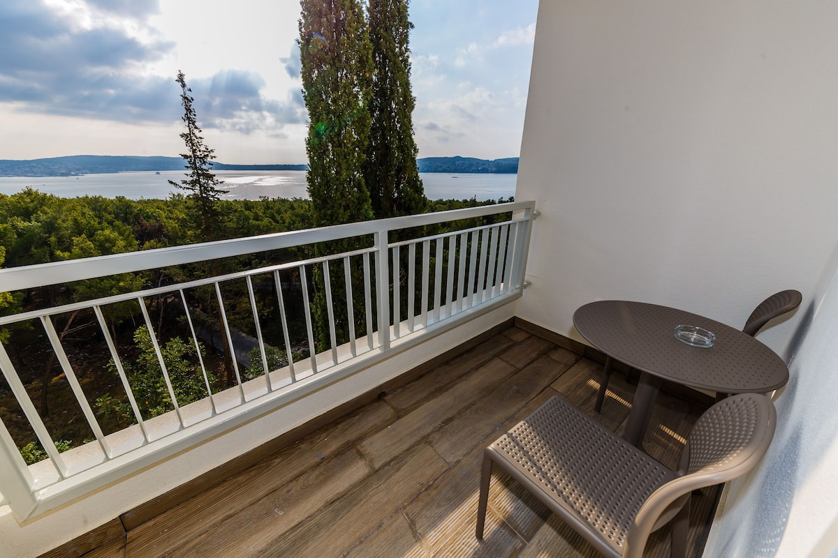 A balcony with a wooden floor, white railing, and a round table with two chairs.