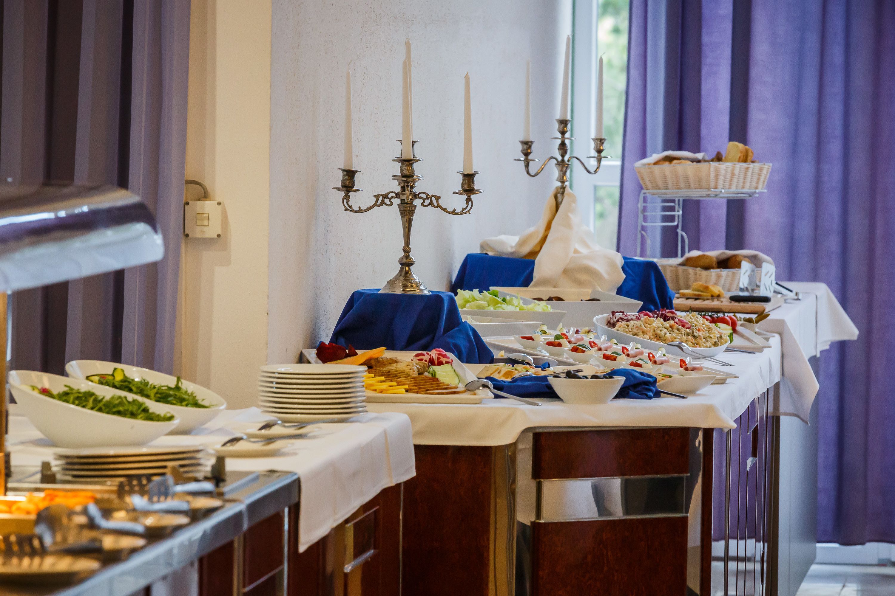 A buffet table with various dishes, a candelabra, and a window with curtains.