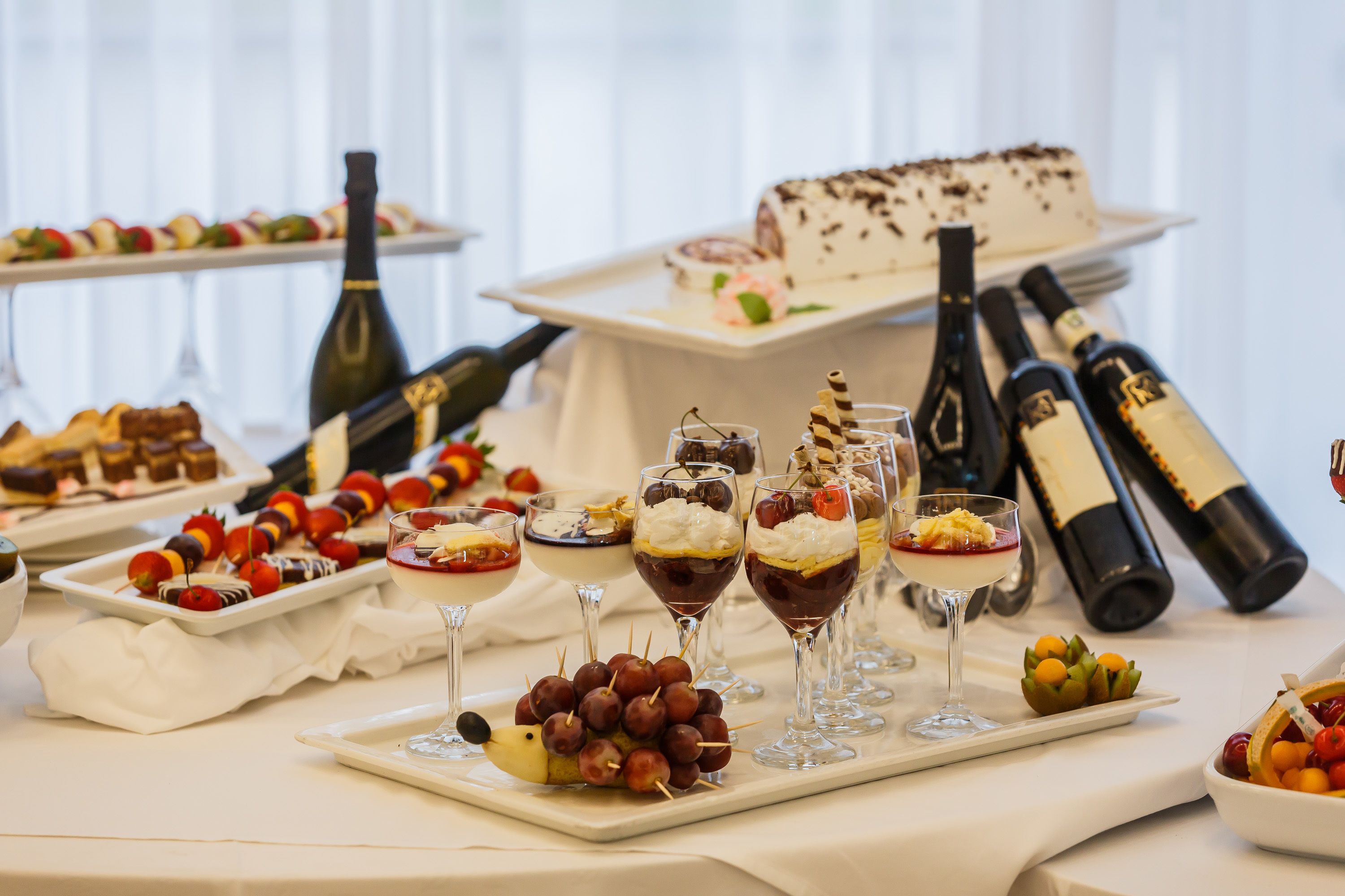 A table with various desserts, wine bottles, and glasses.