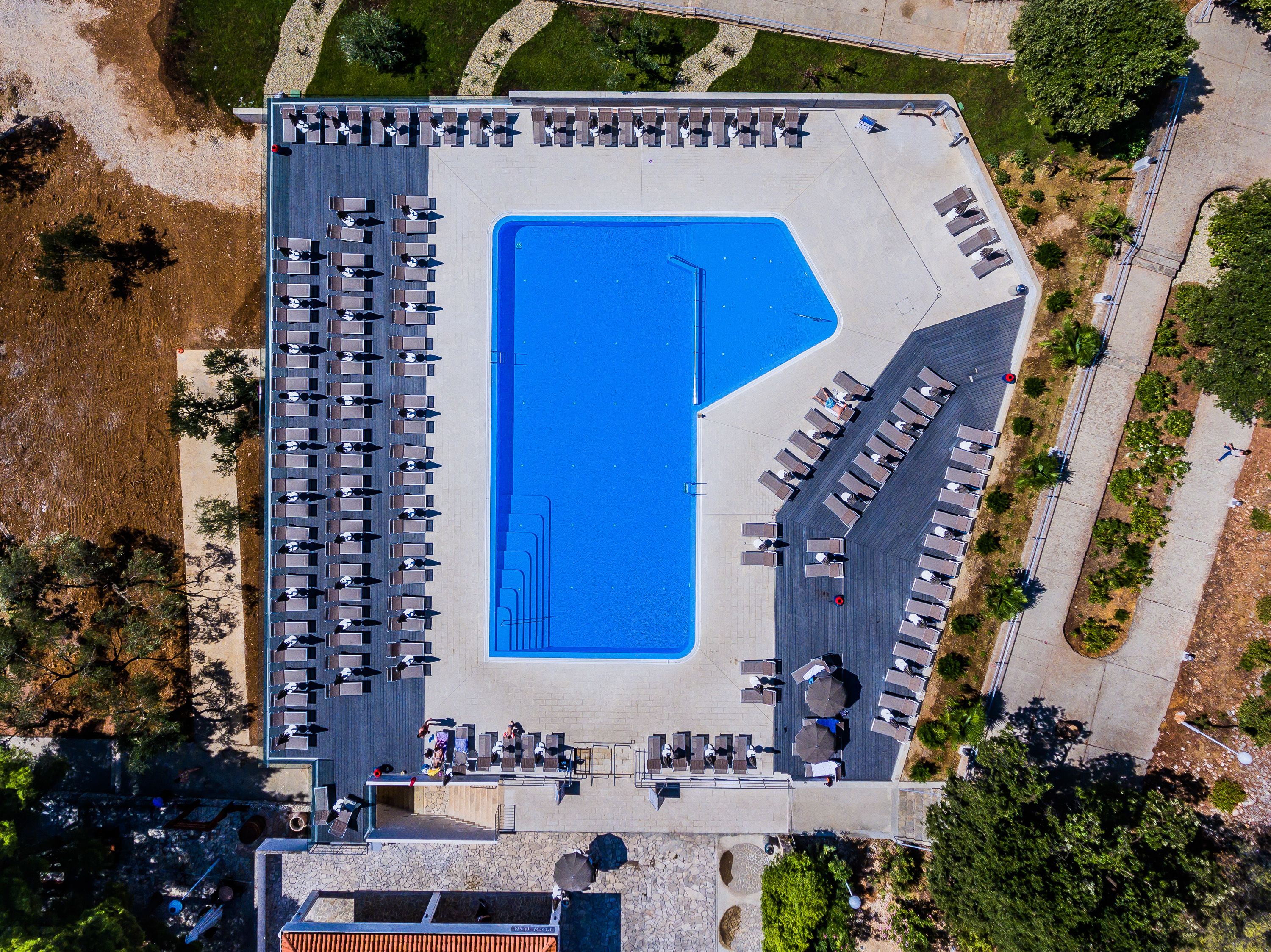 An aerial view of a hotel with a large swimming pool, multiple lounge areas, and a landscaped garden.