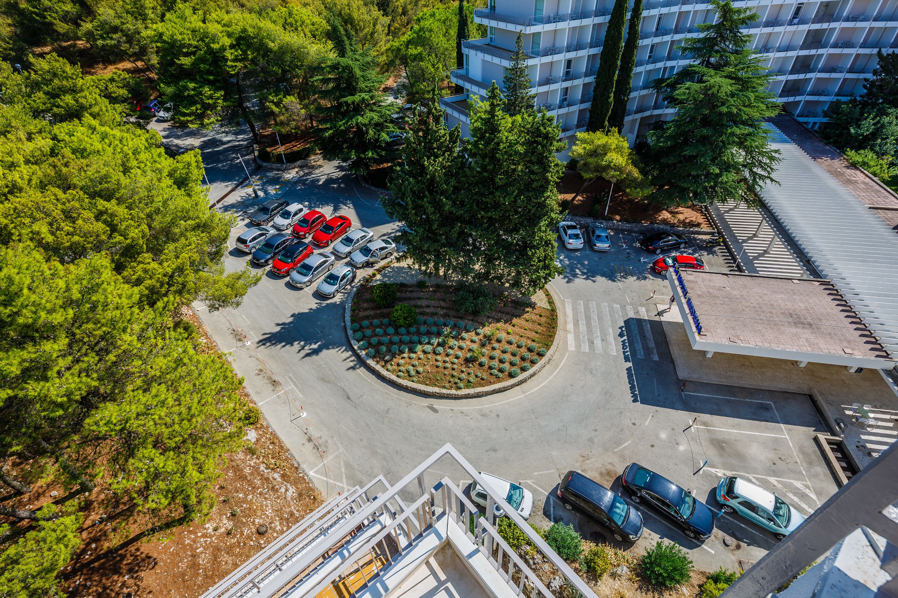 An aerial view of a parking lot with multiple cars, a central landscaped area, and a modern building in the background.