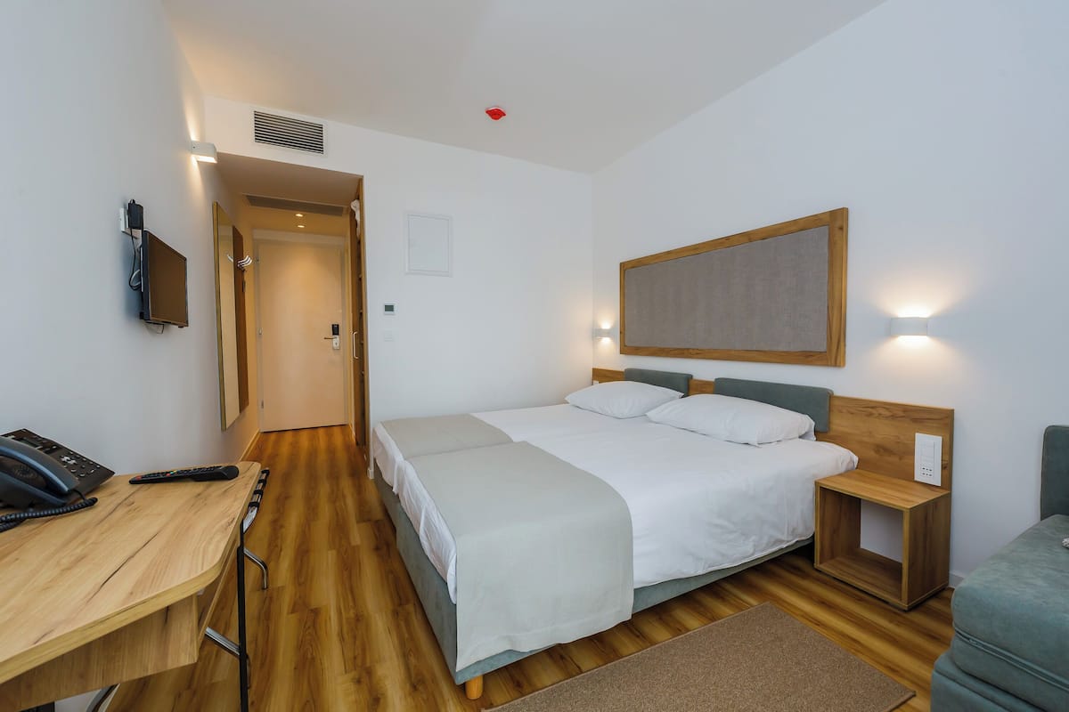 A hotel room with a bed, bedside table, desk with a phone, and a chair.