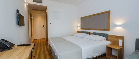 A hotel room with a bed, bedside table, desk with a phone, and a chair.