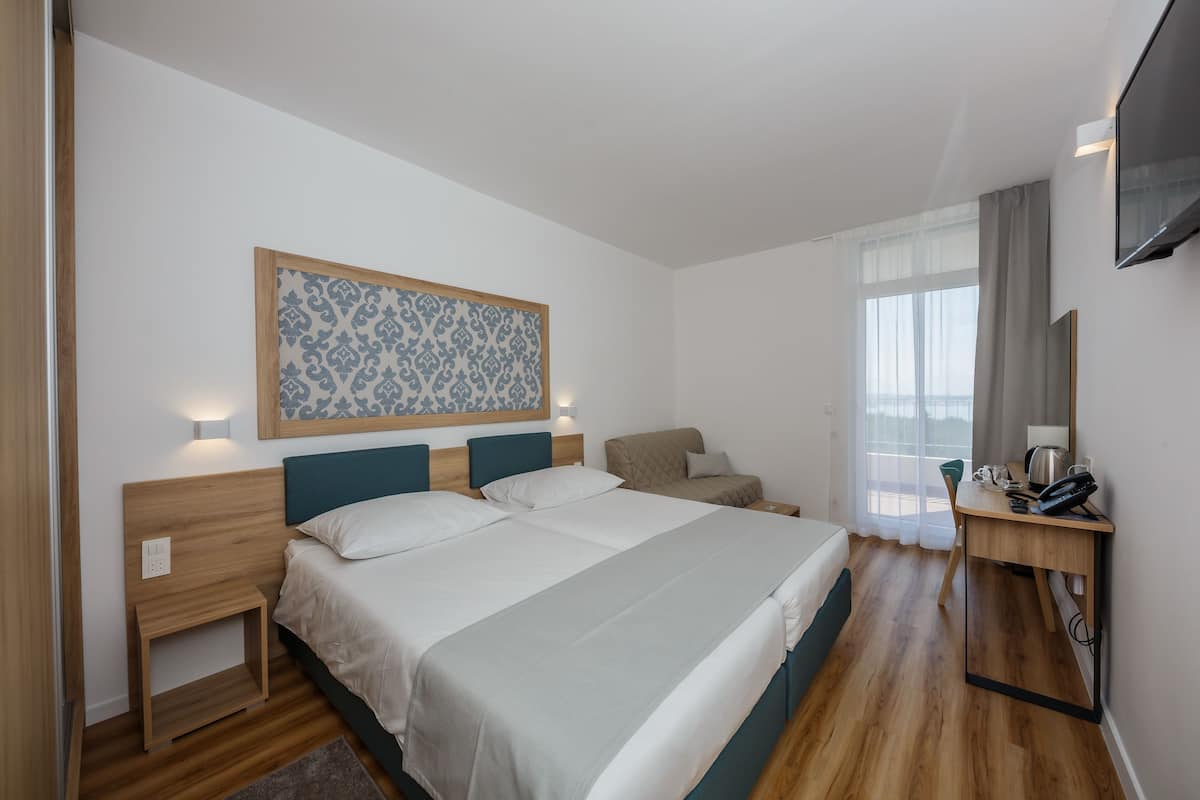 A modern hotel room with a large bed, bedside tables, a desk, and a TV.