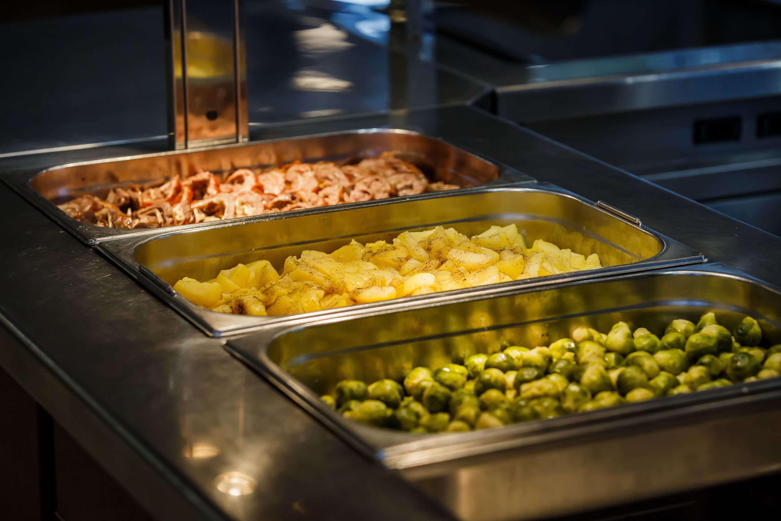 Un buffet con diverse opzioni gastronomiche, tra cui carne, patate e verdure verdi.
