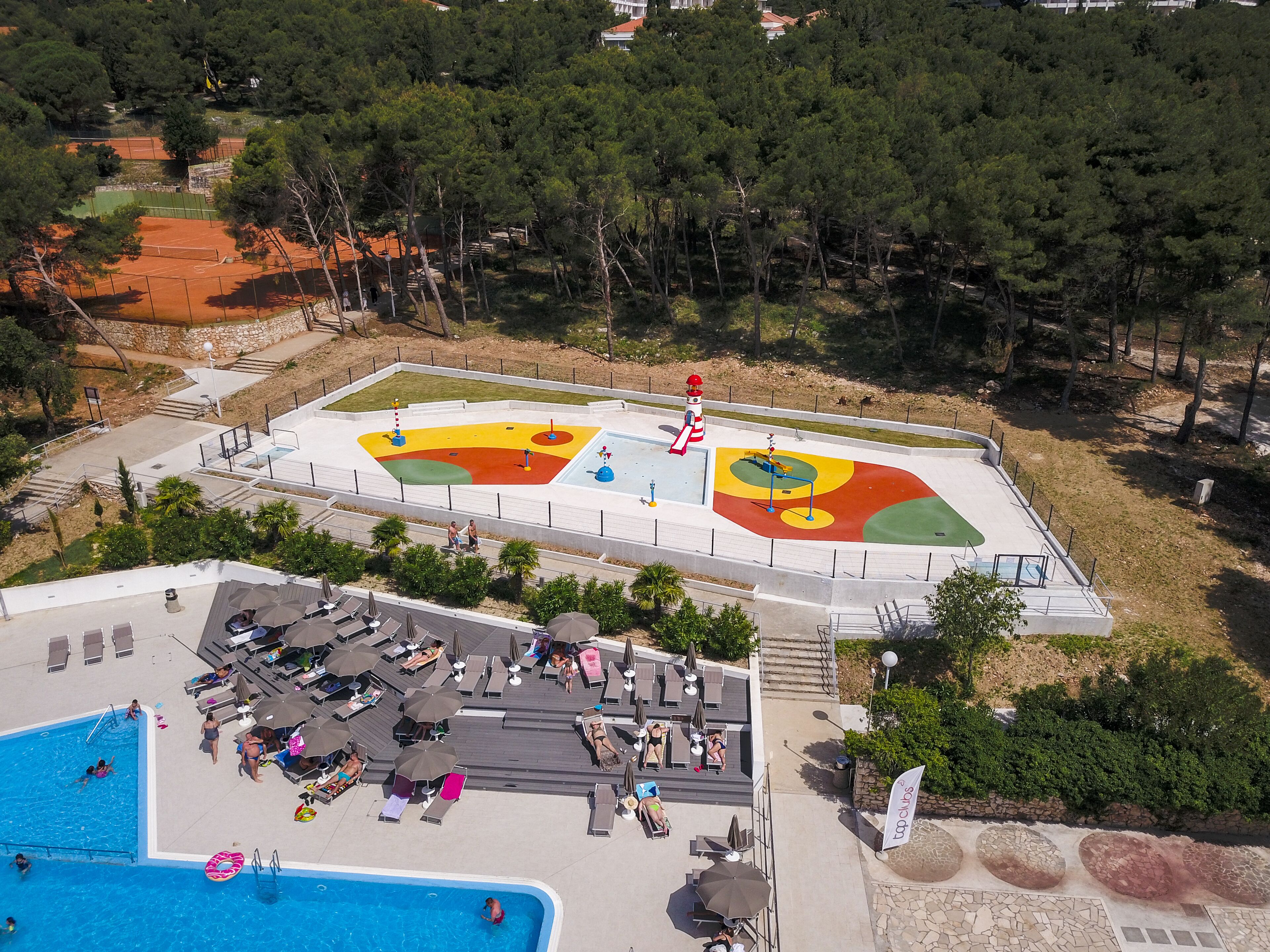 Vue aérienne d’un complexe hôtelier doté d’une piscine, de chaises longues et d’un espace de jeux pour enfants.