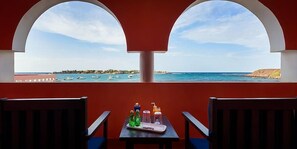 A room with a table and two chairs, a window with a view of the sea and boats, and a red wall. - La Madrague N'gor (Dakar)