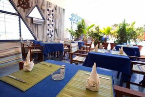 An outdoor restaurant with tables covered in blue tablecloths, wooden chairs, and a nautical-themed wall. - La Madrague N'gor (Dakar)