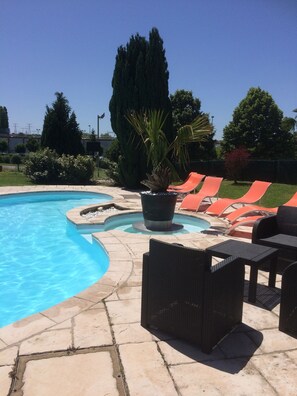 A swimming pool with a stone deck, surrounded by orange lounge chairs and black wicker furniture. - Hôtel La Roselière (Saint-Quentin-Fallavier)