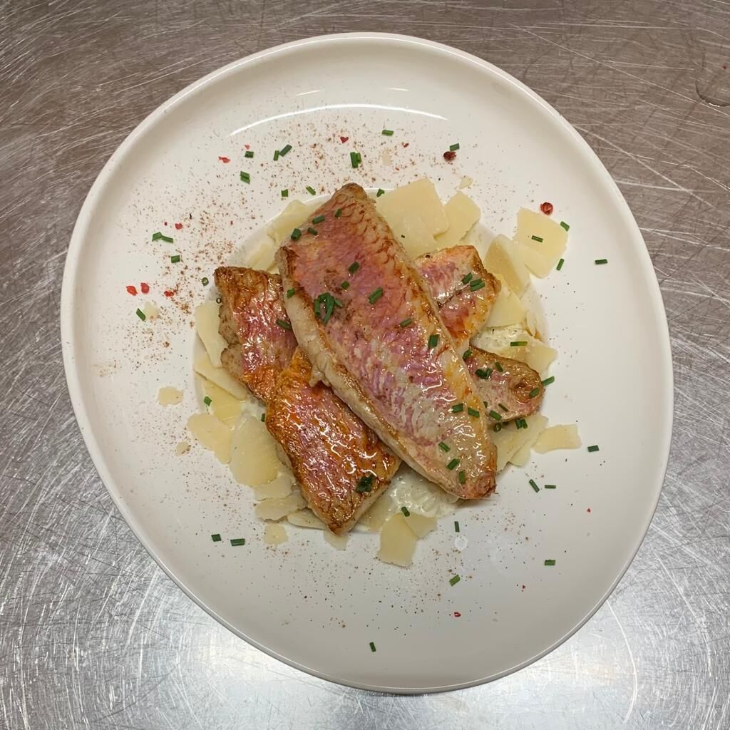 A white plate with a piece of grilled fish, some chopped chives, and a sprinkle of red pepper flakes.