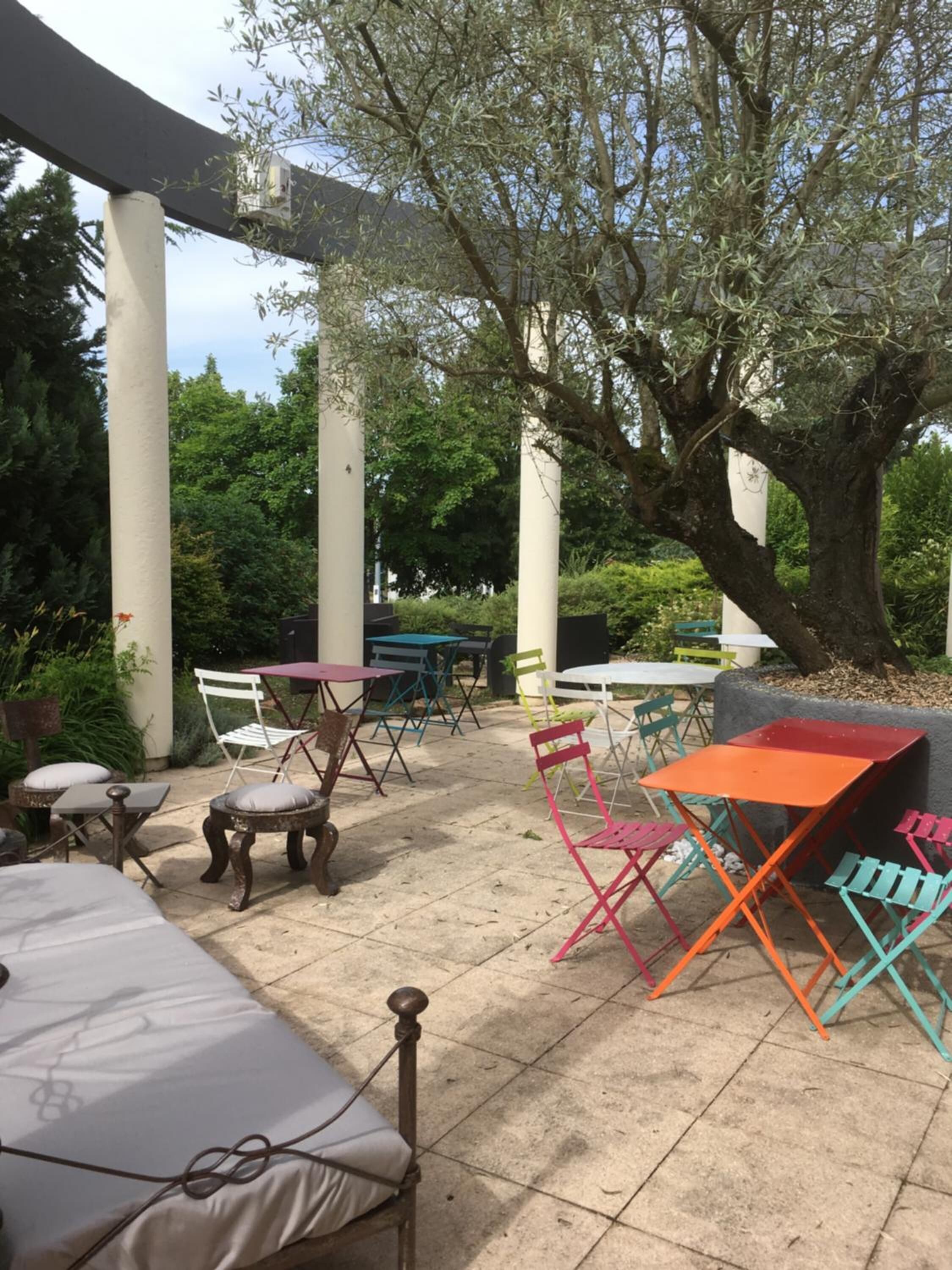 Un patio al aire libre con mesas y sillas, rodeado de árboles y follaje.
