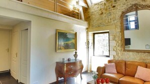 A spacious living area with a high ceiling, a stone wall, a wooden bench, a sofa, a coffee table, and a painting on the wall.