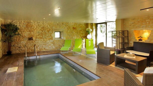 A spa area with a pool, green lounge chairs, wicker furniture, stone walls, and a large window.