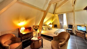 A cozy attic bedroom with a bed, a TV, and a desk with a lamp and books.