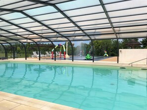 A swimming pool with a covered area, lounge chairs, and a water play structure. - CAMPING CAMPILO (La Roche-sur-Yon)