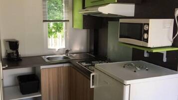 Une cuisine compacte équipée d’une cuisinière à gaz, d’un four à micro-ondes, d’un évier et d’une fenêtre avec des stores.