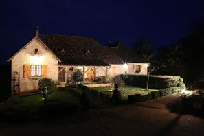 A stone house with a tiled roof, a porch, and a well-lit garden at night. - Chambres d'Hotes Larnaudie (Coly-Saint-Amand)